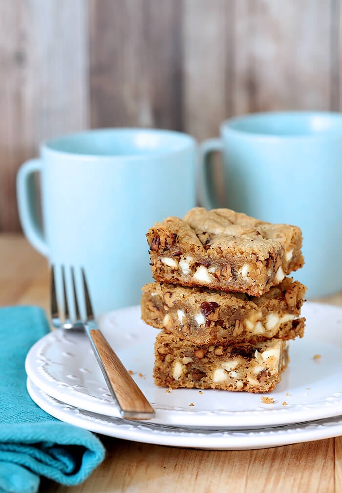 Blondies with White Chocolate Chips and Toasted Pecans on a White Plate with Aqua Coffee Mugs in Background