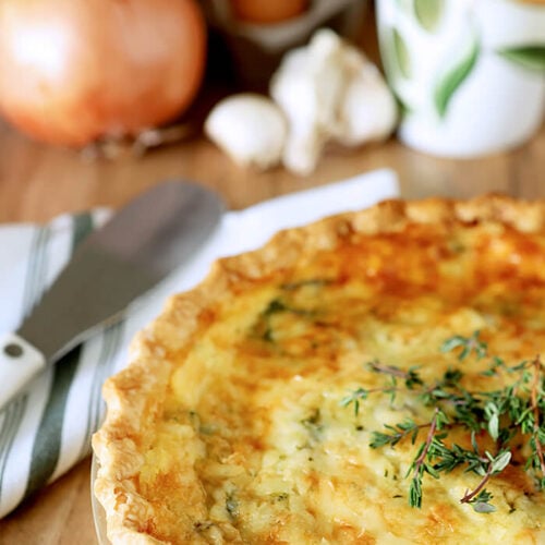 Spinach, Onion, and Mushroom Quiche in a White Pie Plate on a Table with a Green and White Napkin and a Serving Knife.