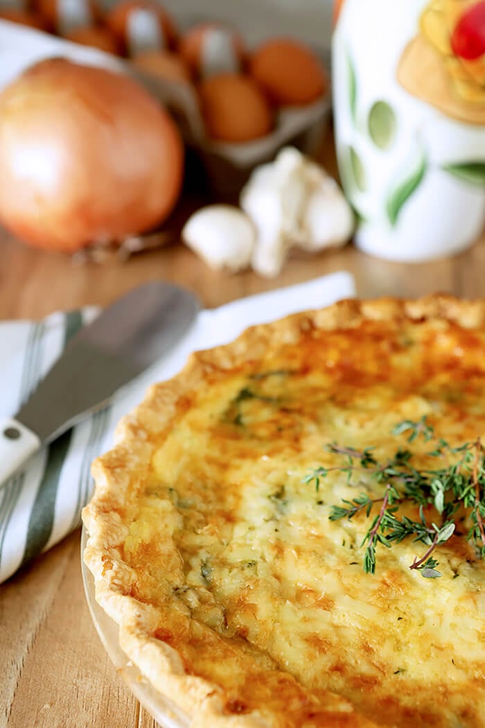 Spinach, Onion, and Mushroom Quiche in a White Pie Plate on a Table with a Green and White Napkin and a Serving Knife.