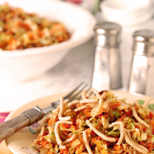 A serving of Asian Slaw with Almonds on a serving plate with colorful pink and green napkin.