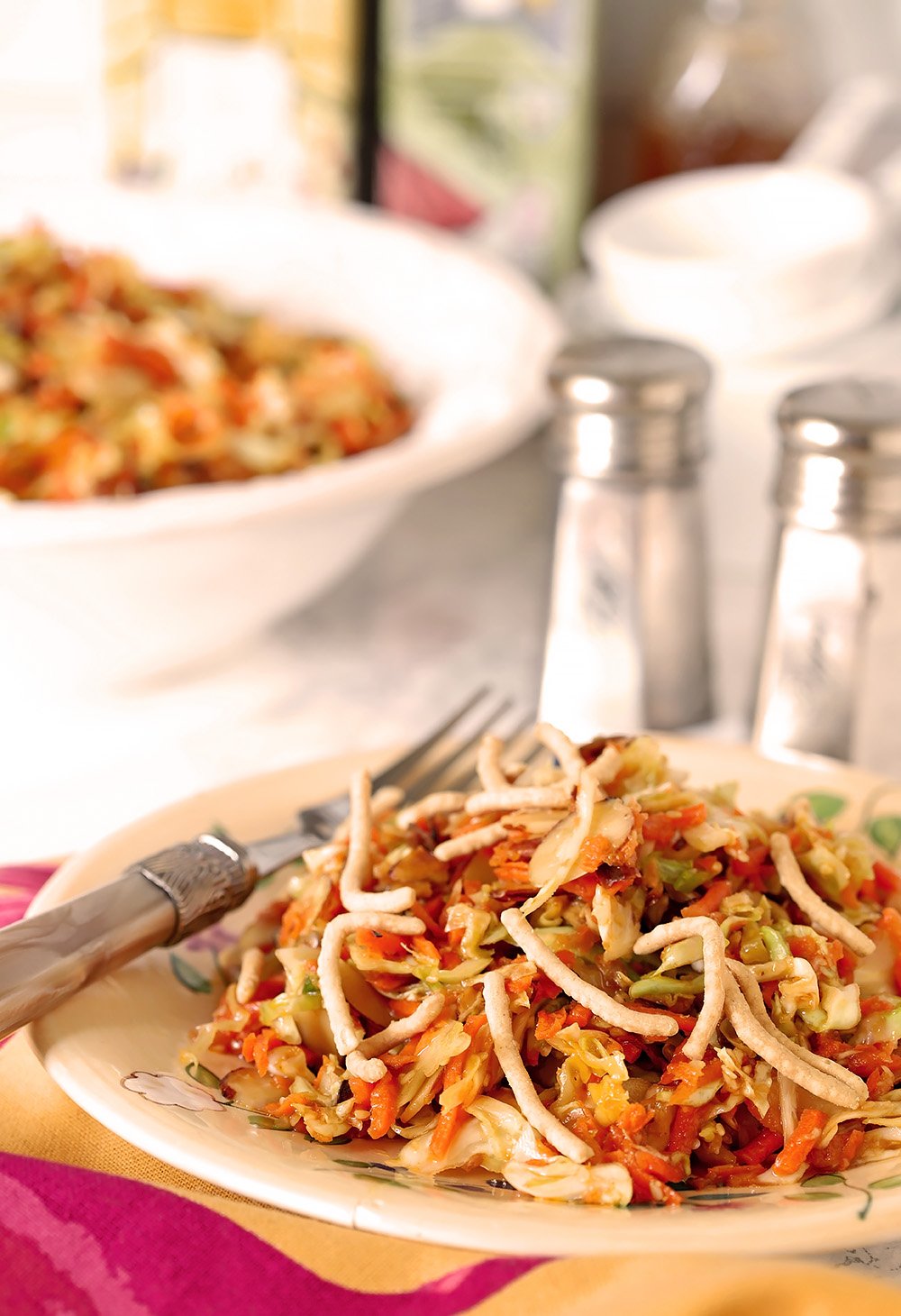 A serving of Asian Slaw with Almonds on a serving plate with colorful pink and green napkin.