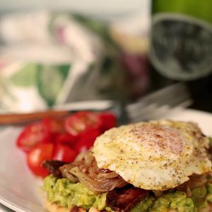 Avocado Toast with Bacon and Egg on Naan Served with Cherry Tomatoes on a White Plate