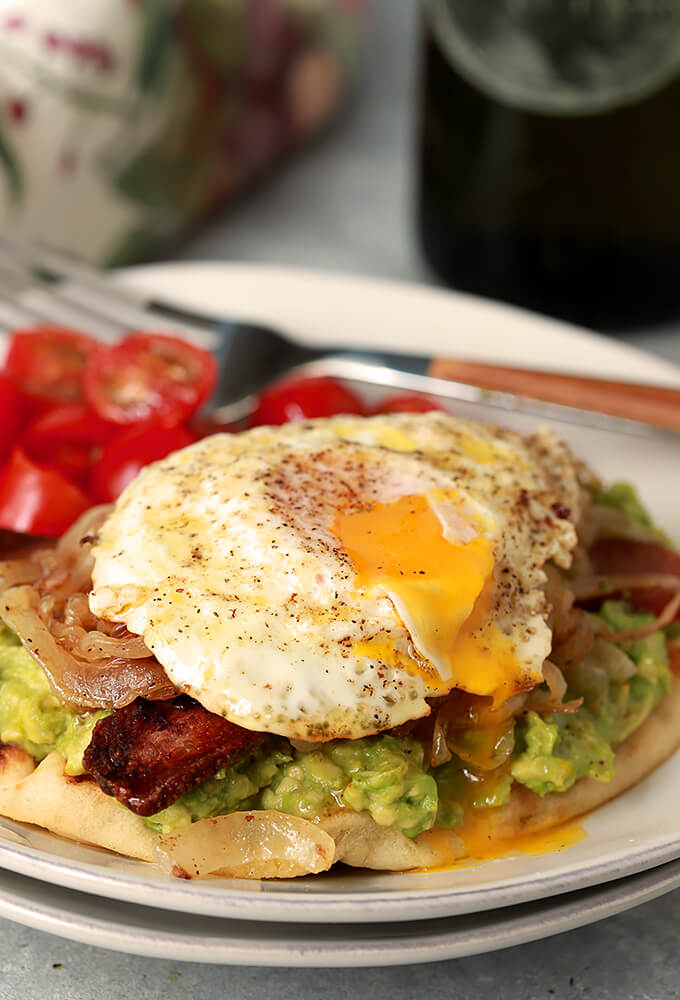 Avocado Toast with Bacon and Egg on Naan Served on a White Plate with Cherry Tomatoes