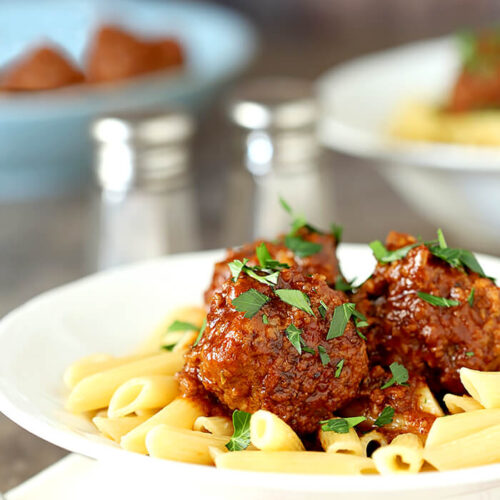 Beef Meatballs with Bourbon in tomato sauce sit on pasta in a white bowl.