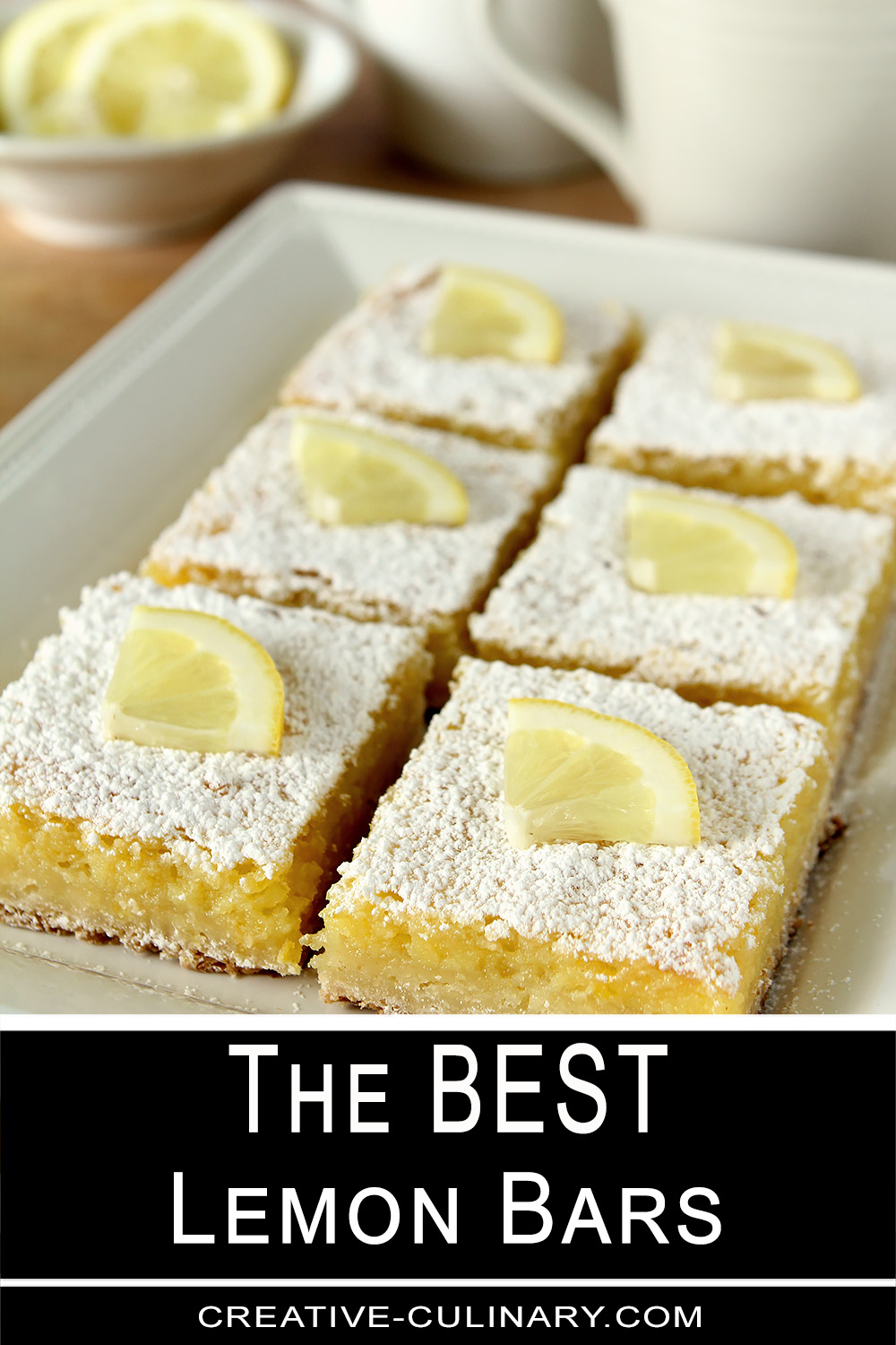 A plate of lemon bars cut into squares and topped with powdered sugar and a quarter slice of lemon.