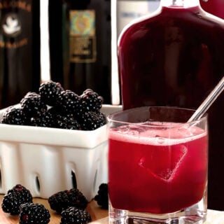 Homemade Blackberry Liqueur (Creme de Mure) in a flask bottle with fresh blackberries on display and a simple cocktail.