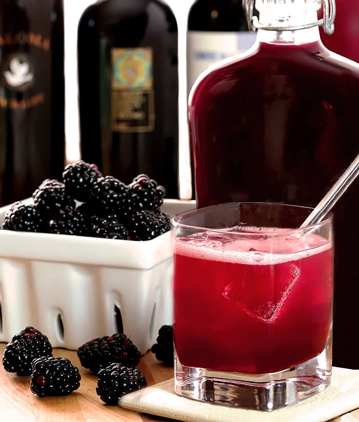 Homemade Blackberry Liqueur (Creme de Mure) in a flask bottle with fresh blackberries on display and a simple cocktail.