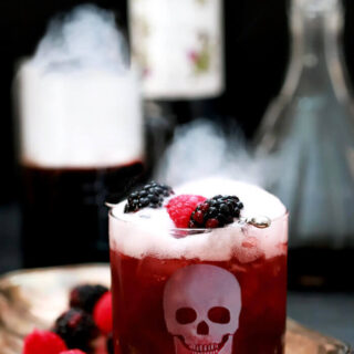 Sparkling Blackberry Smash Halloween Cocktail Served in a Glass with an Etched Skull and Dry Ice