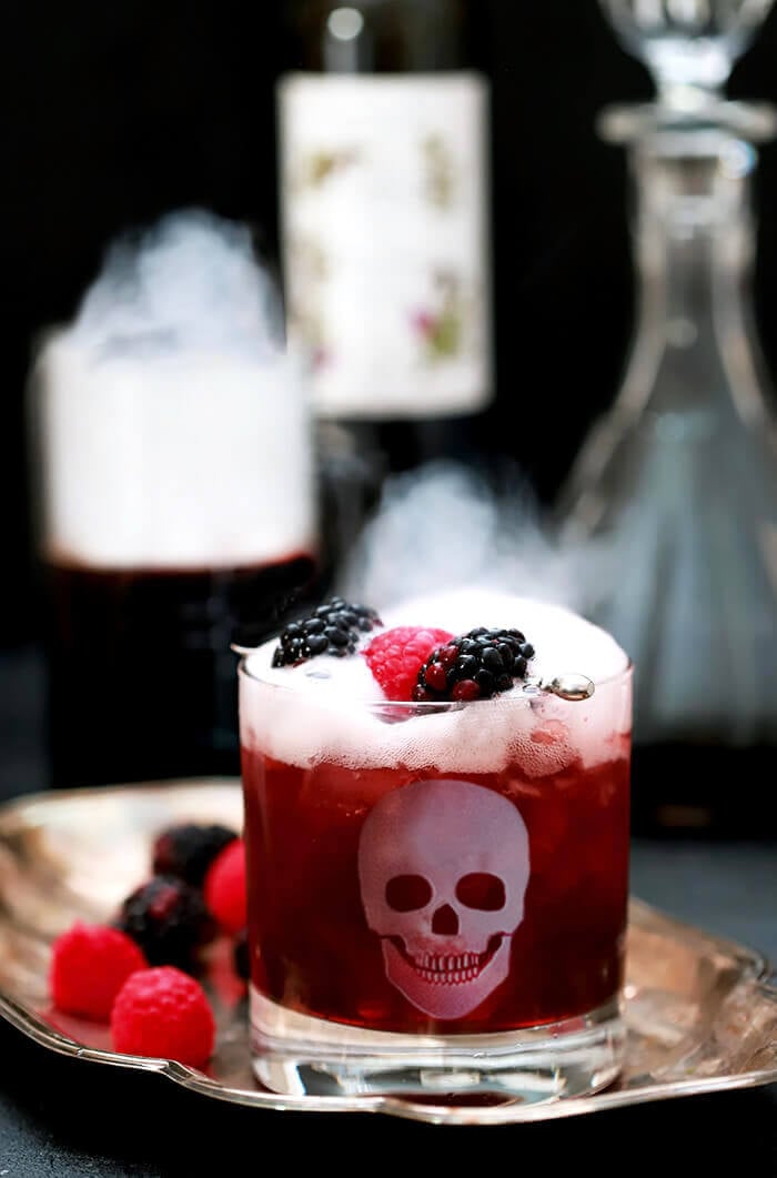 Best Halloween Cocktail Recipes - Sparkling Blackberry Smash Halloween Cocktail Served in a Glass with an Etched Skull and Dry Ice