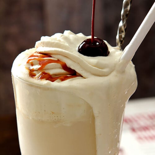 Boozy Salted Caramel Milkshake served in a tall glass, drizzled with caramel and topped with whipped cream and a cherry.