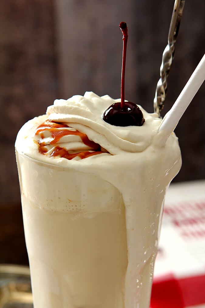 Boozy Salted Caramel Milkshake served in a tall glass, drizzled with caramel and topped with whipped cream and a cherry.