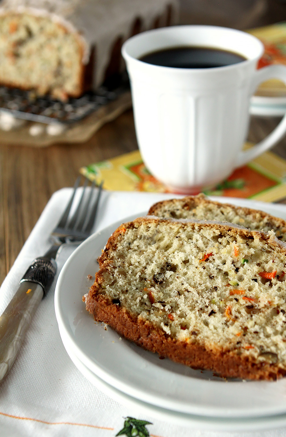 Slice of Carrot Zucchini Bread on White Plate with a Cup of Coffee.