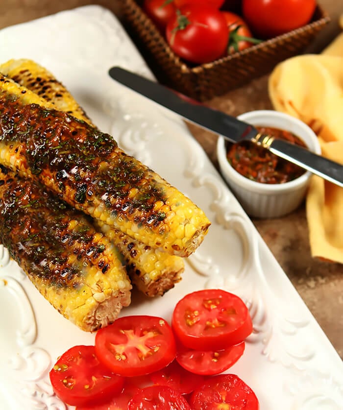 Platter of Cilantro, Honey, and Chile Corn on the Cob Served with a Warm Taco on a White Plate with Tomatoe Slices