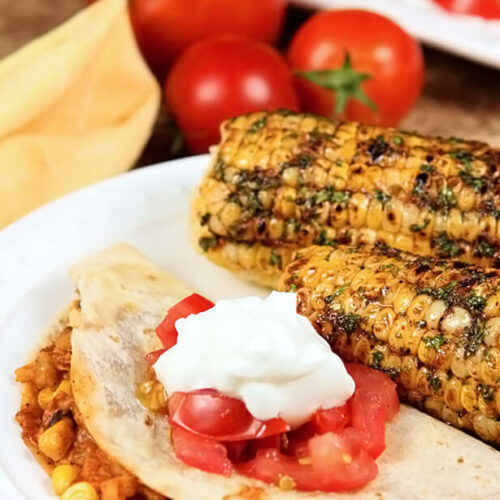 Cilantro, Honey, and Chile Corn on the Cob Served with a Warm Taco on a White Plate