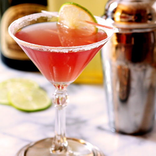 Cosmopolitan Cocktail on Marble Surface with Cocktail Shaker in Background.