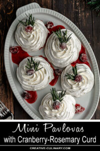 Mini Pavlovas with Cranberry Curd and Whipped Cream, garnished with Sugared Cranberries and a Sprig of Rosemary