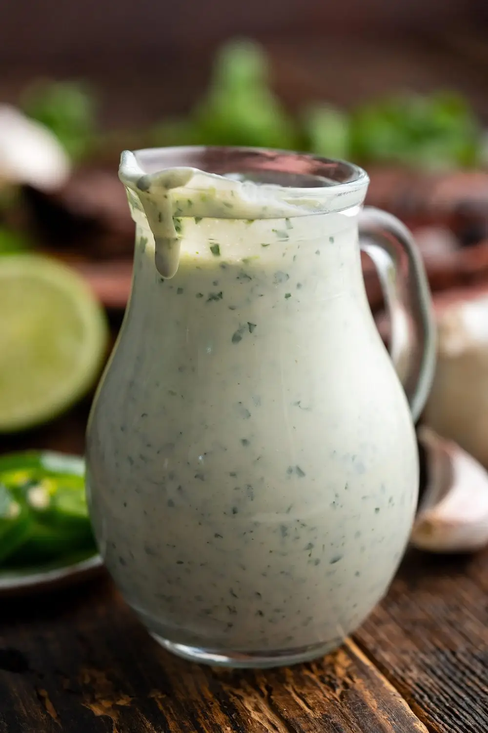 Creamy Cilantro Sauce in glass carafe with Ingredients in background including lime, jalapeno, and cilantro.