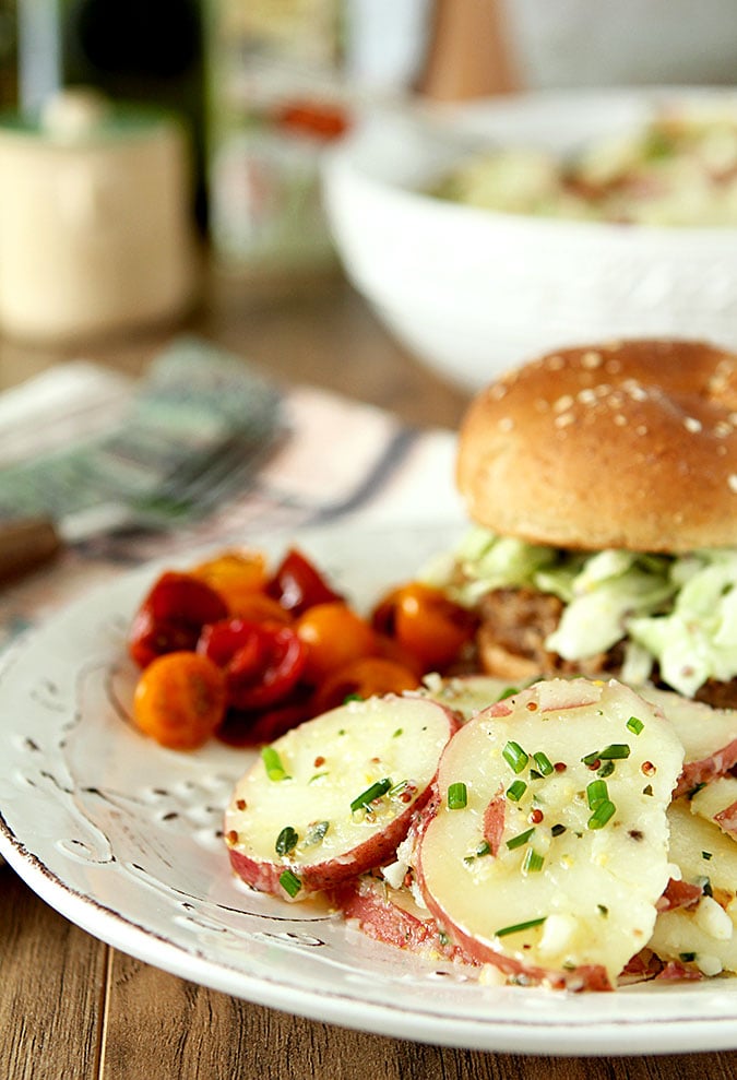 French Potato Salad with Herbs on a White Plate with a Sandwich and Chopped Tomatoes