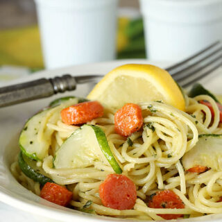 Garlic Pesto Pasta with Carrots and Zucchini Served with a Lemon Wedge in a White Bowl