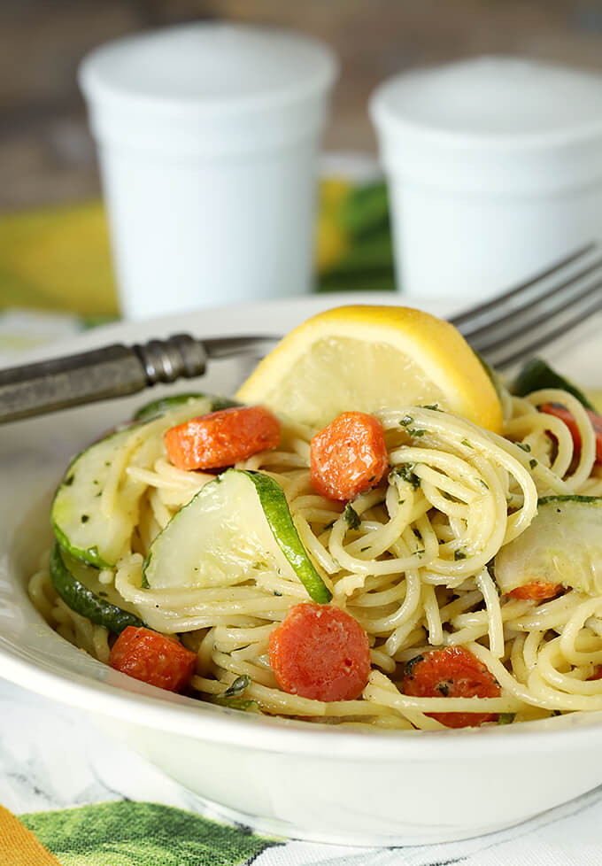 Garlic Pesto Pasta with Carrots and Zucchini Served with a Lemon Wedge in a White Bowl