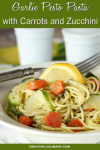 Garlic Pesto Pasta with Carrots & Zucchini Served on a White Plate with Lemon Garnish