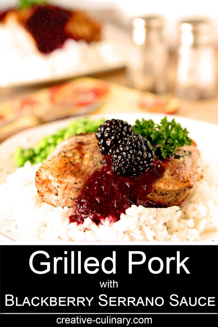 Grilled Pork on a white plate topped with Blackberry Serrano Sauce and garnished with parsley.