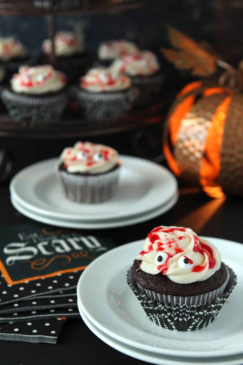 Halloween Mummy Cupcakes with chocolate cake, buttercream frosting and red simple syrup drizzled over frosting and candy eyes.