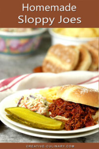 Homemade Sloppy Joes on White Plate with Chips, Slaw, and Pickles