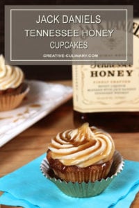 Closeup of Jack Daniels Honey Whiskey Cupcakes with a Boozy Drizzle from a Spoon In a Metallic Cupcake Liner in Front of a Bottle of Jack Daniels Tennessee Honey