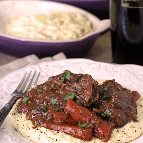 Italian Pot Roast with Carrots is Served over Polenta on a White Plate.