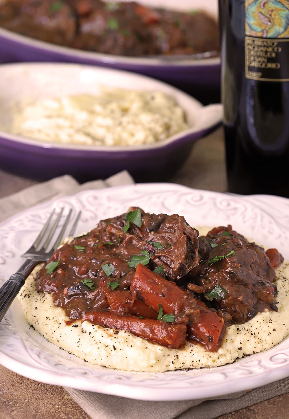 Italian Pot Roast with Carrots is Served over Polenta on a White Plate.