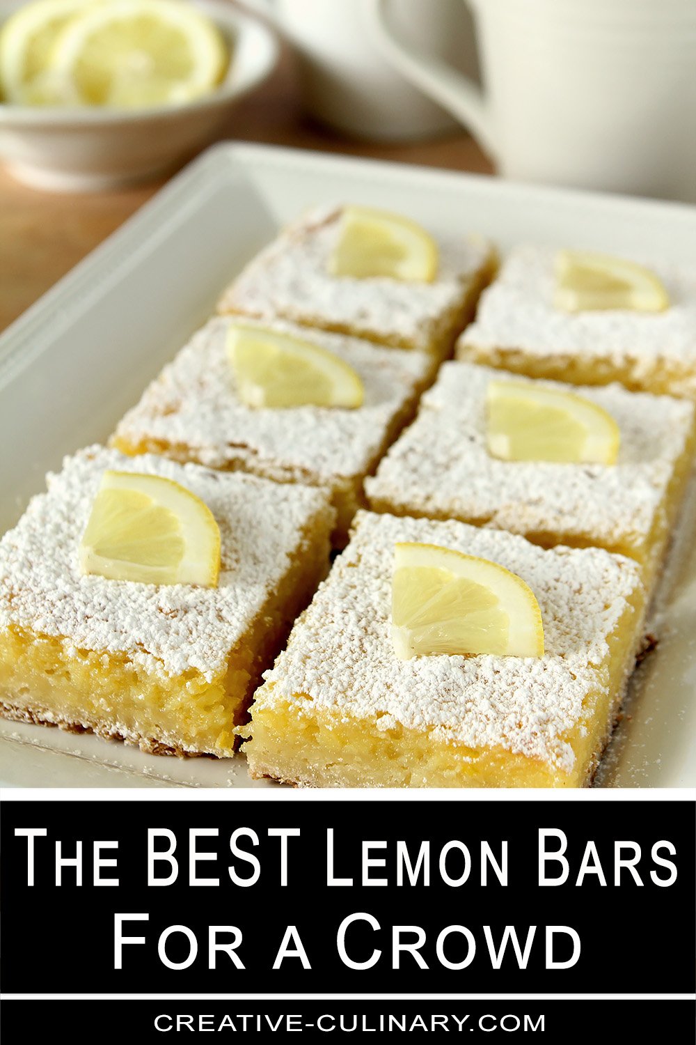 A plate of lemon bars cut into squares and topped with powdered sugar and a quarter slice of lemon.