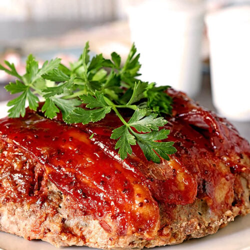 Meatloaf with Bacon and Sausage and a Sweet Chili Glaze on a Serving Plate and Garnished with a Sprig of Parsley