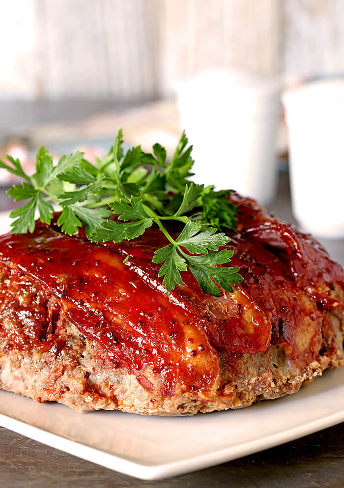 Meatloaf with Bacon and Sausage and a Sweet Chili Glaze on a Serving Plate and Garnished with a Sprig of Parsley