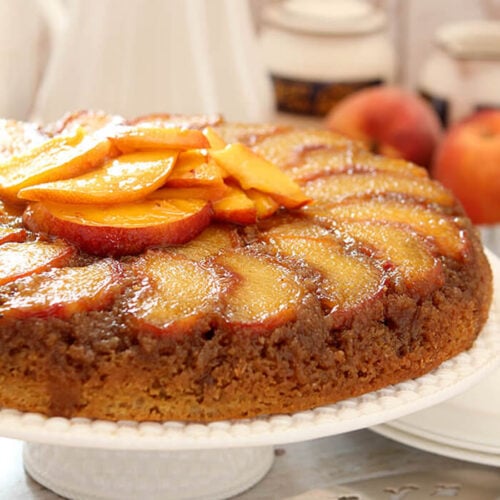 Fresh Peach Upside Down Cake on a White Cake Platter with More Peaches as Garnish