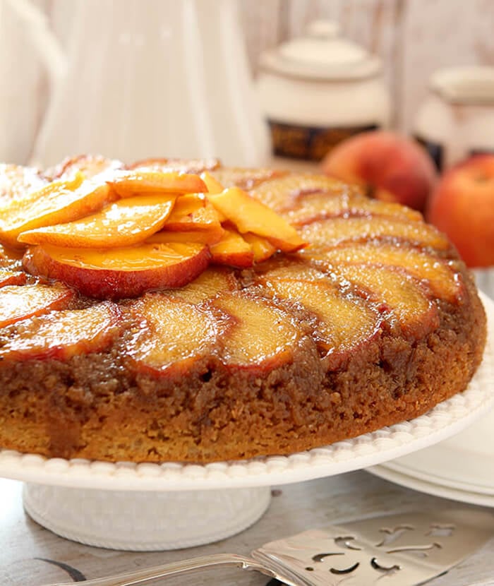 Fresh Peach Upside Down Cake on a White Cake Platter with More Peaches as Garnish