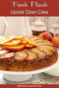 Fresh Peach Upside Down Cake on a White Cake Platter with More Peaches as Garnish