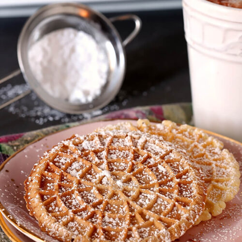 Pizzelles - Italian Waffle Cookies Sprinkled with Powdered Sugar and Served on Pink Plate