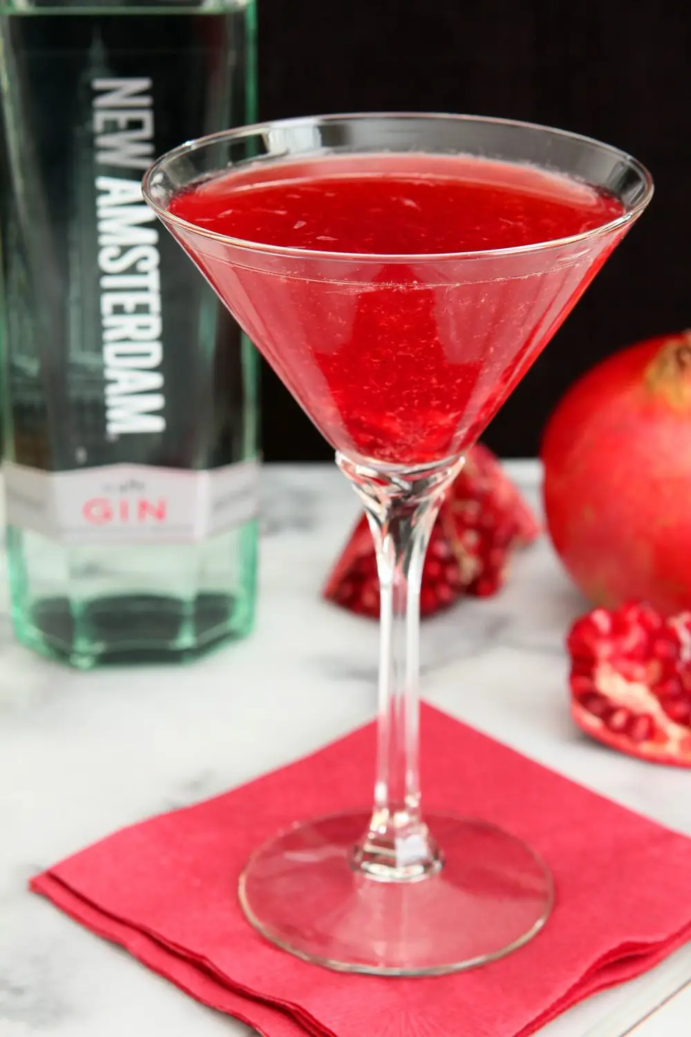 Gin and Pomegranate Cocktail Served with Pomegranate and Bottle of Gin in background.