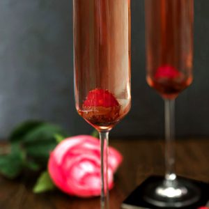 Sparkling Rosé Wine is poured int glasses decorated with chocolate and fresh raspberries.