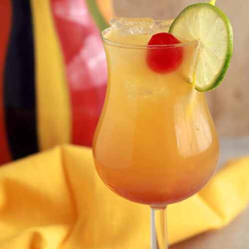 Classic Rum Punch Cocktail combines rum, pineapple juice and orange juice in a glass garnished with a maraschino cherry and a lime wheel.