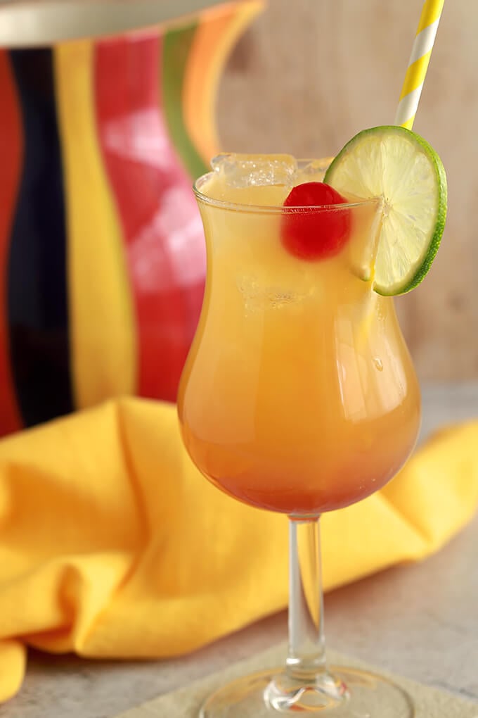 Classic Rum Punch Cocktail combines rum, pineapple juice and orange juice in a glass garnished with a maraschino cherry and a lime wheel.