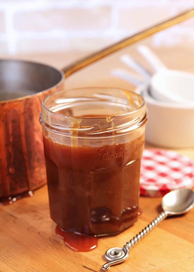 Jar of Homemade Salted Caramel Sauce Sitting Next to a Copper Pan with a Decorative Spoon on the Table