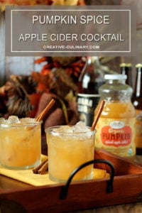 Pumpkin Spiced Apple Cider Cocktail in a Lowball Glass on a Wood and Wrought Iron Tray with Bottles of Rum and Cider in the Background