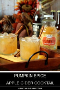 Pumpkin Spiced Apple Cider Cocktail in a Lowball Glass on a Wood and Wrought Iron Tray with Bottles of Rum and Cider in the Background