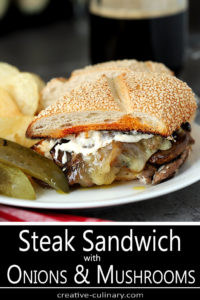 Steak and Cheese Sandwich with Caramelized Onions and Mushrooms Topped with Horseradish Mayo and Served on a White Plate with Pickles and Chips